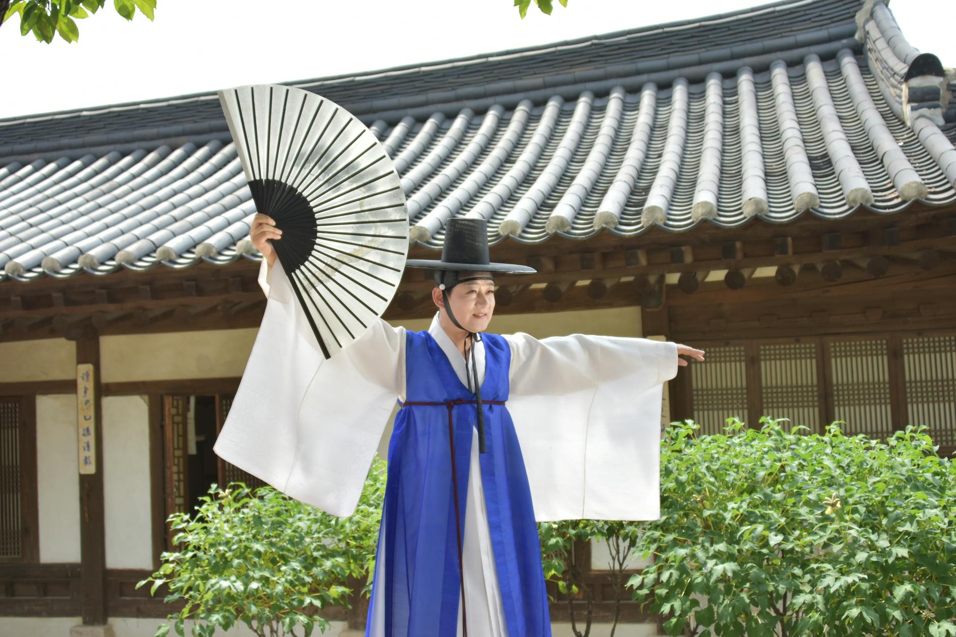 A person in traditional Korean clothing performs a cultural dance with a fan outdoors.