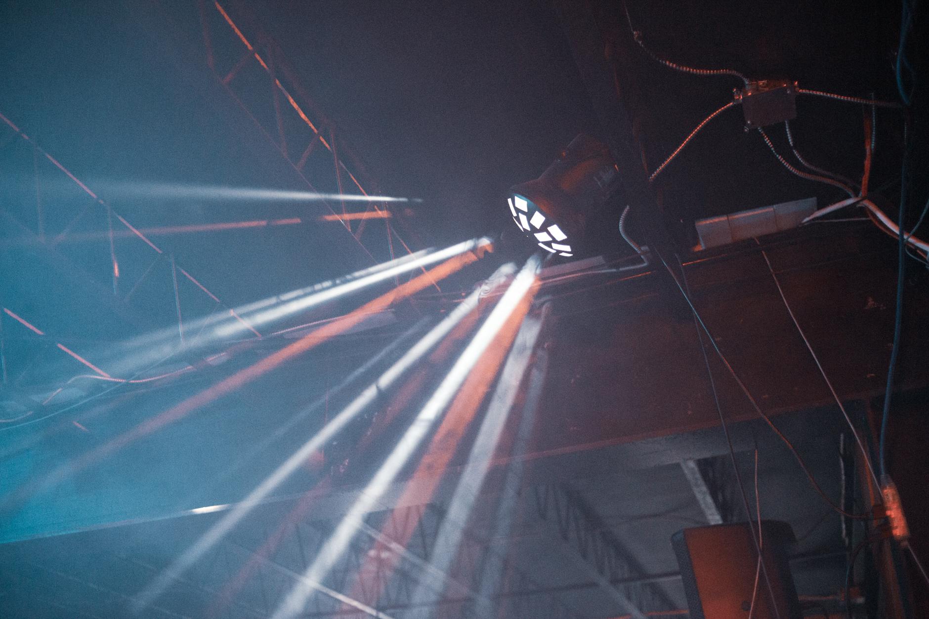 Illuminated light beams create dramatic effects against an industrial ceiling.
