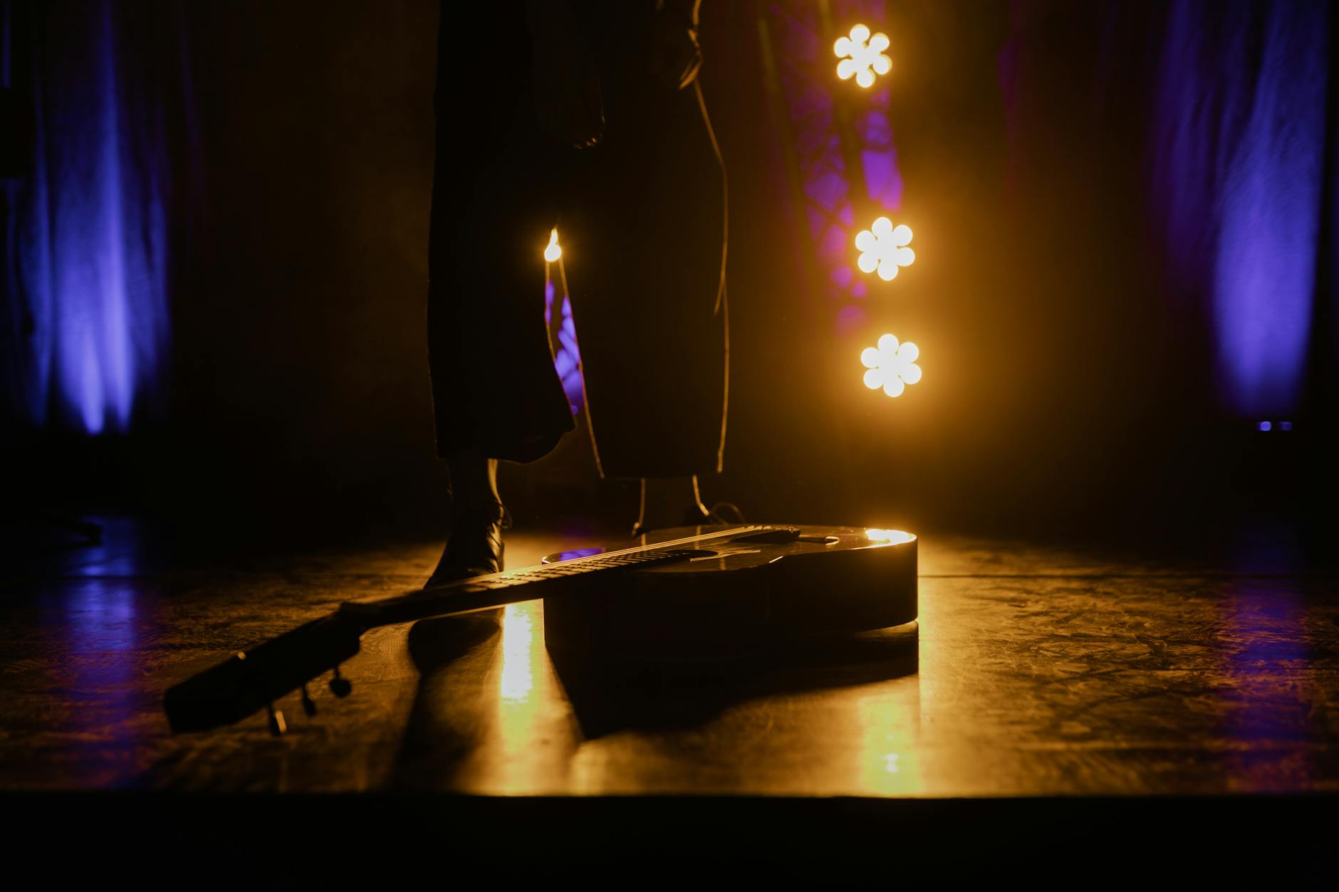 An acoustic guitar lies on stage with dramatic lighting creating a moody atmosphere.