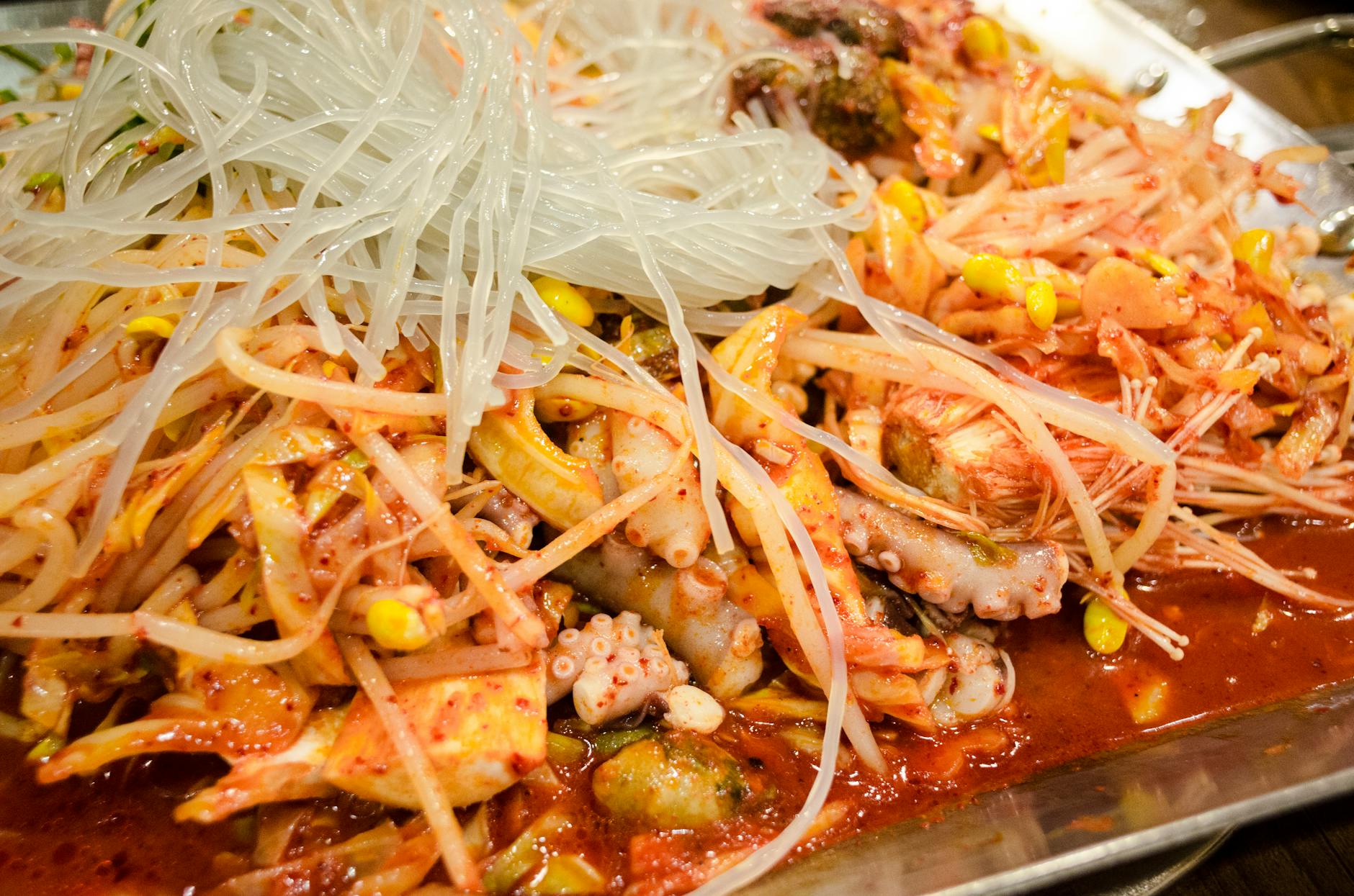 Close-up of a vibrant Korean seafood and noodle dish with kimchi.