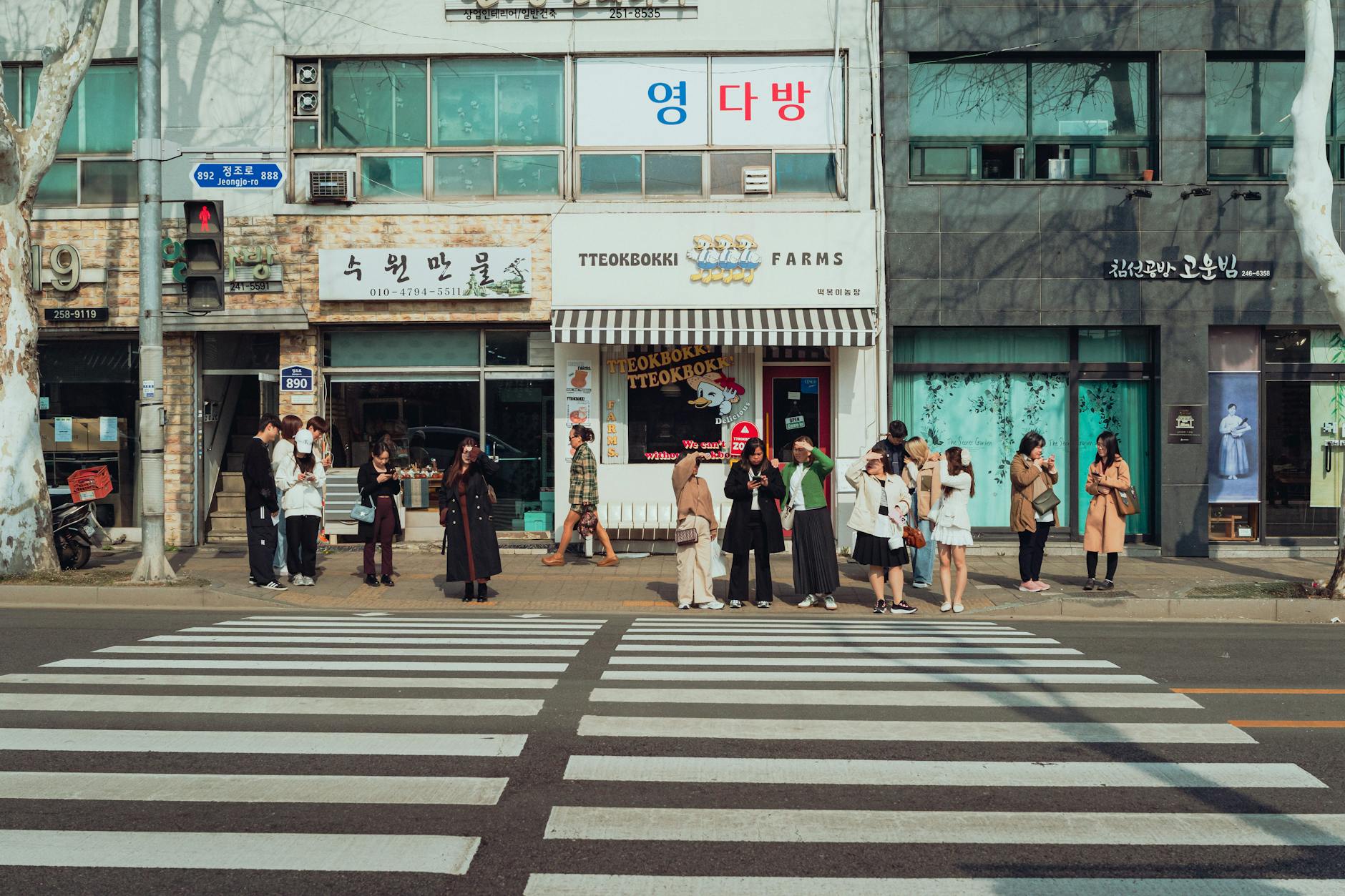 Pedestrians waiting at a crosswalk in Suwon-si, showcasing local architecture and culture.