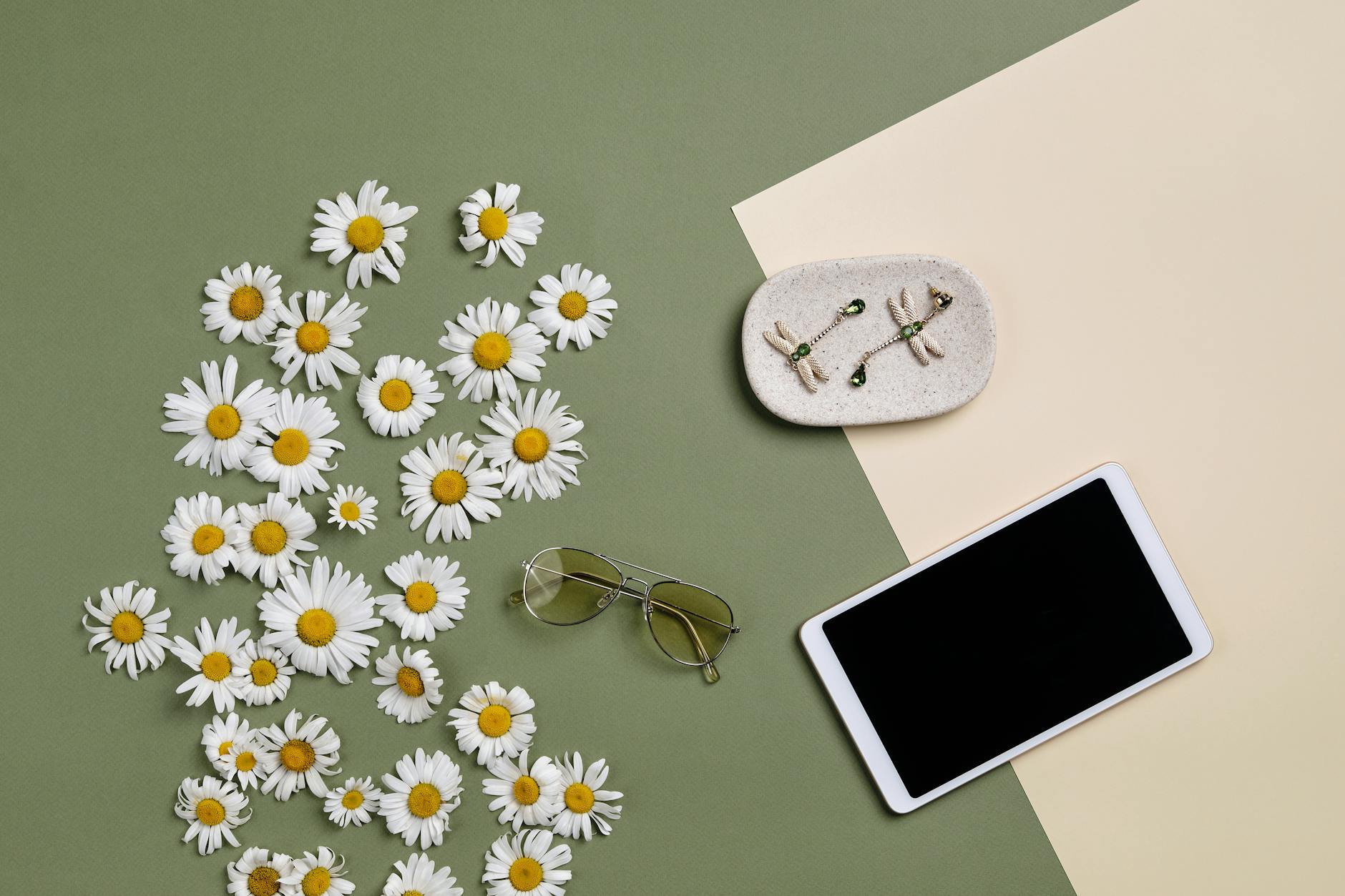 Chic flat lay featuring yellow daisies, sunglasses, tablet, and earrings on a two-tone background.
