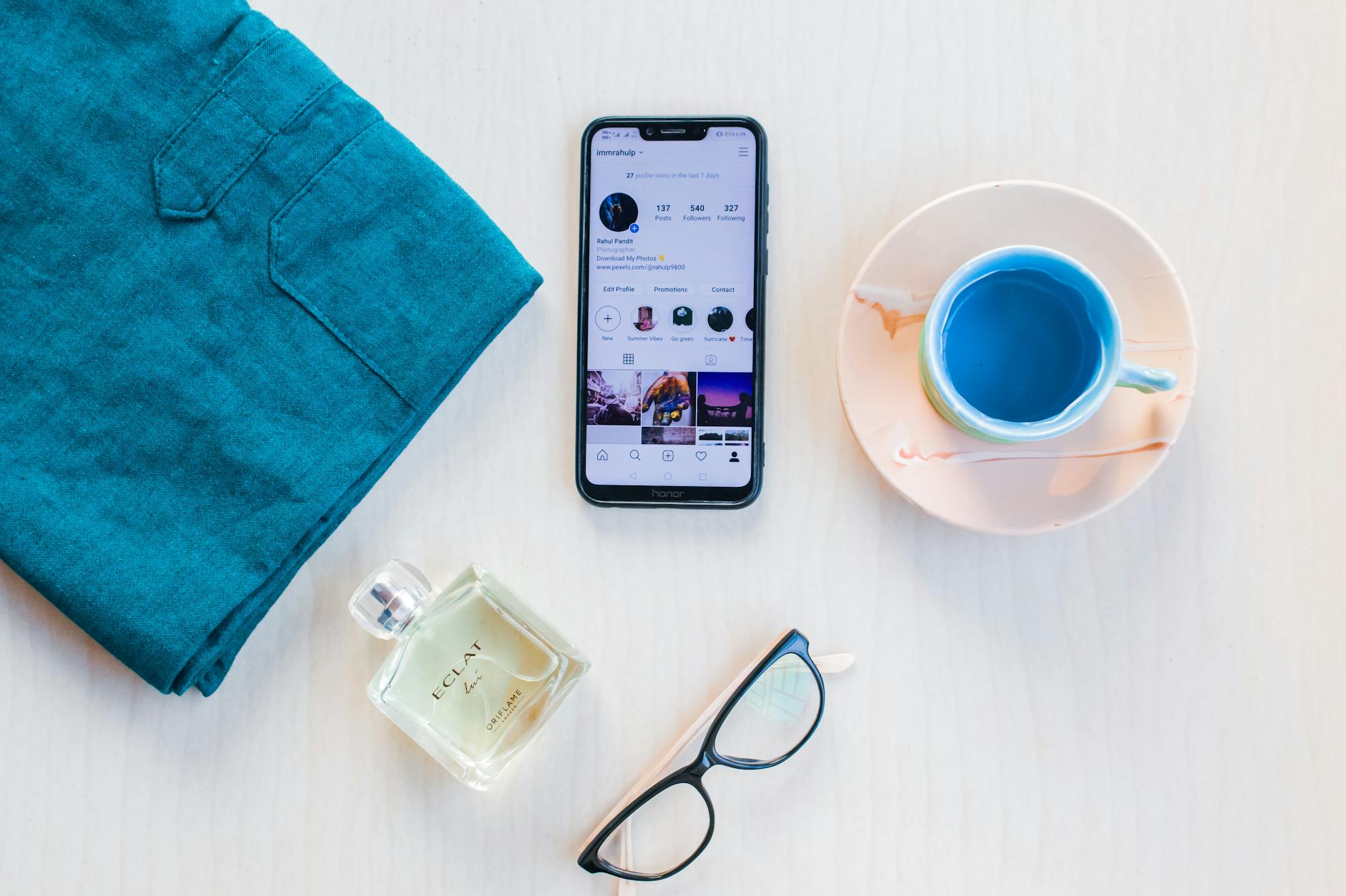From above of modern cellphone with images on screen near mug of colorful drink and bottle of perfume